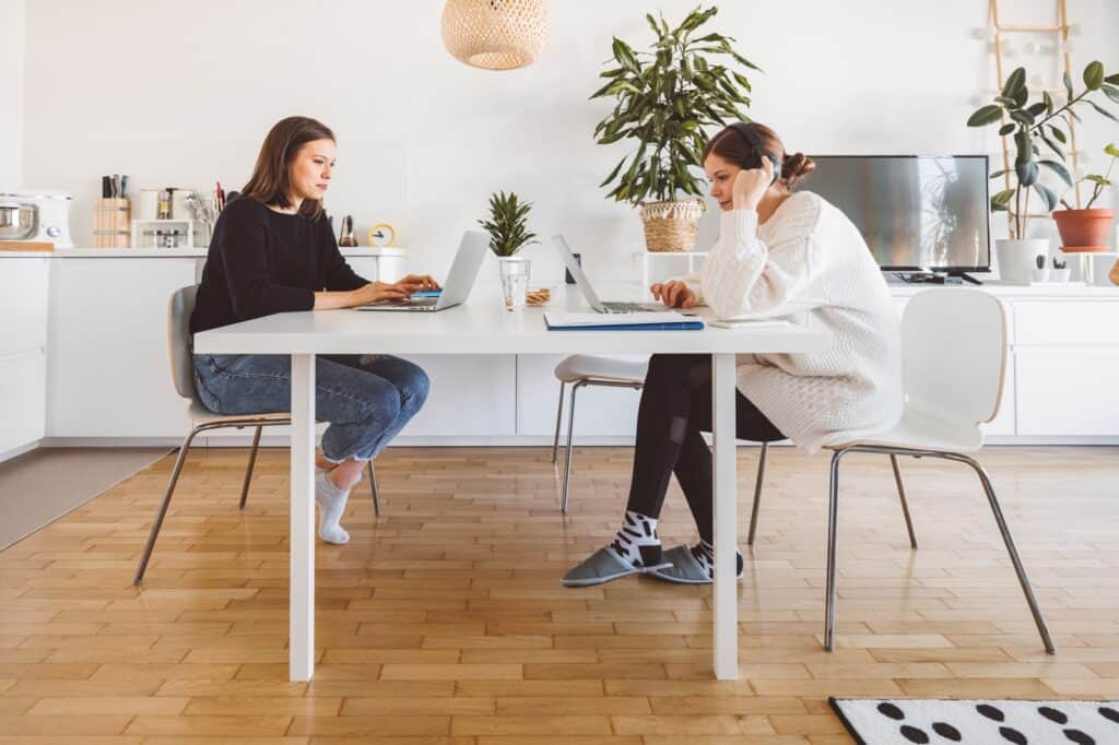 Two female roommates in front of their laptops in the kitchen