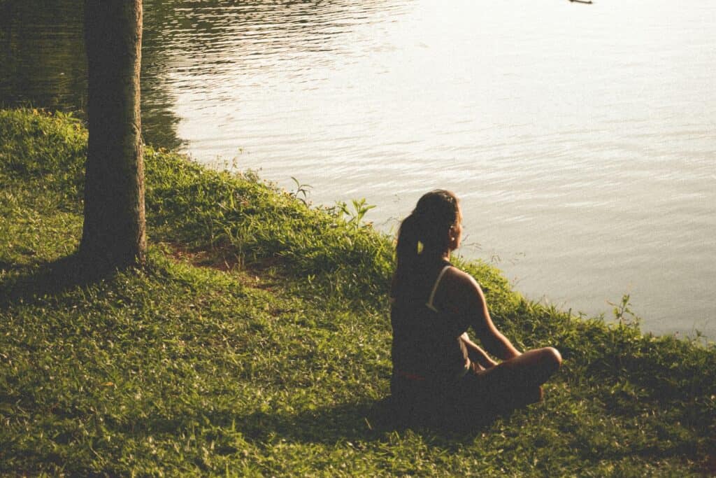 A woman is sitting at the side of the lake in a park