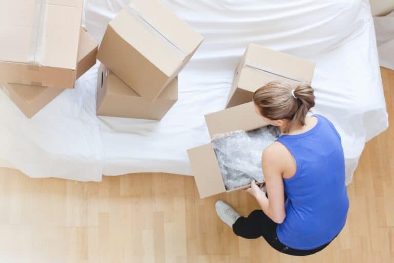 A woman is moving boxes in her new flat and a couch is still covered in the concept of 'how to save money when moving to Hounslow'.