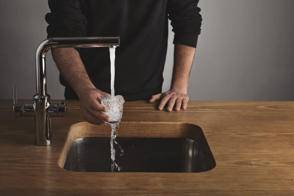 Cropped image of a man pouring water from the faucet into a glass