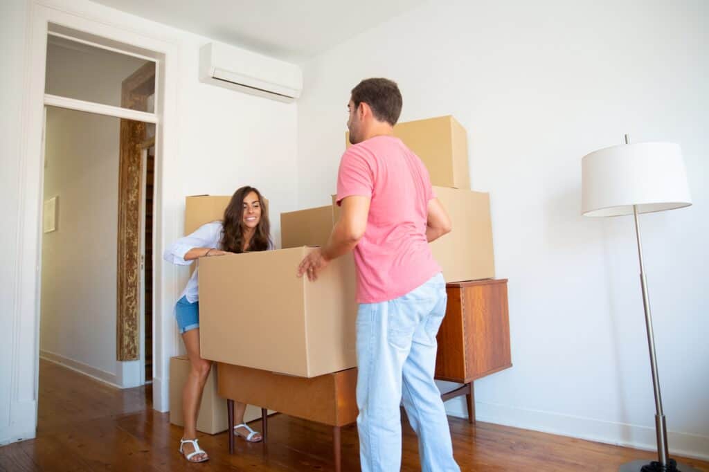 A happy young couple carrying a box during the move in the concept of 'Changing Address and Updating Utilities After Moving to Hounslow'.