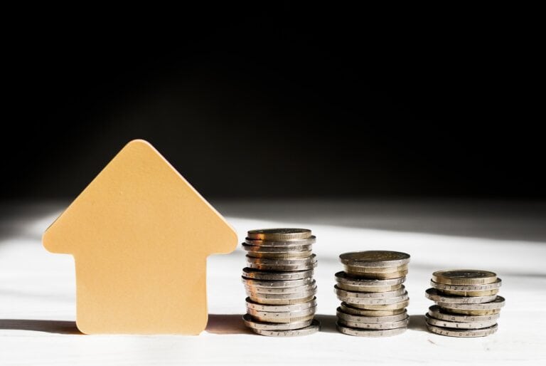 A house-shaped tile and stacks of coins in the concept of 'Hounslow Removals Cost'.